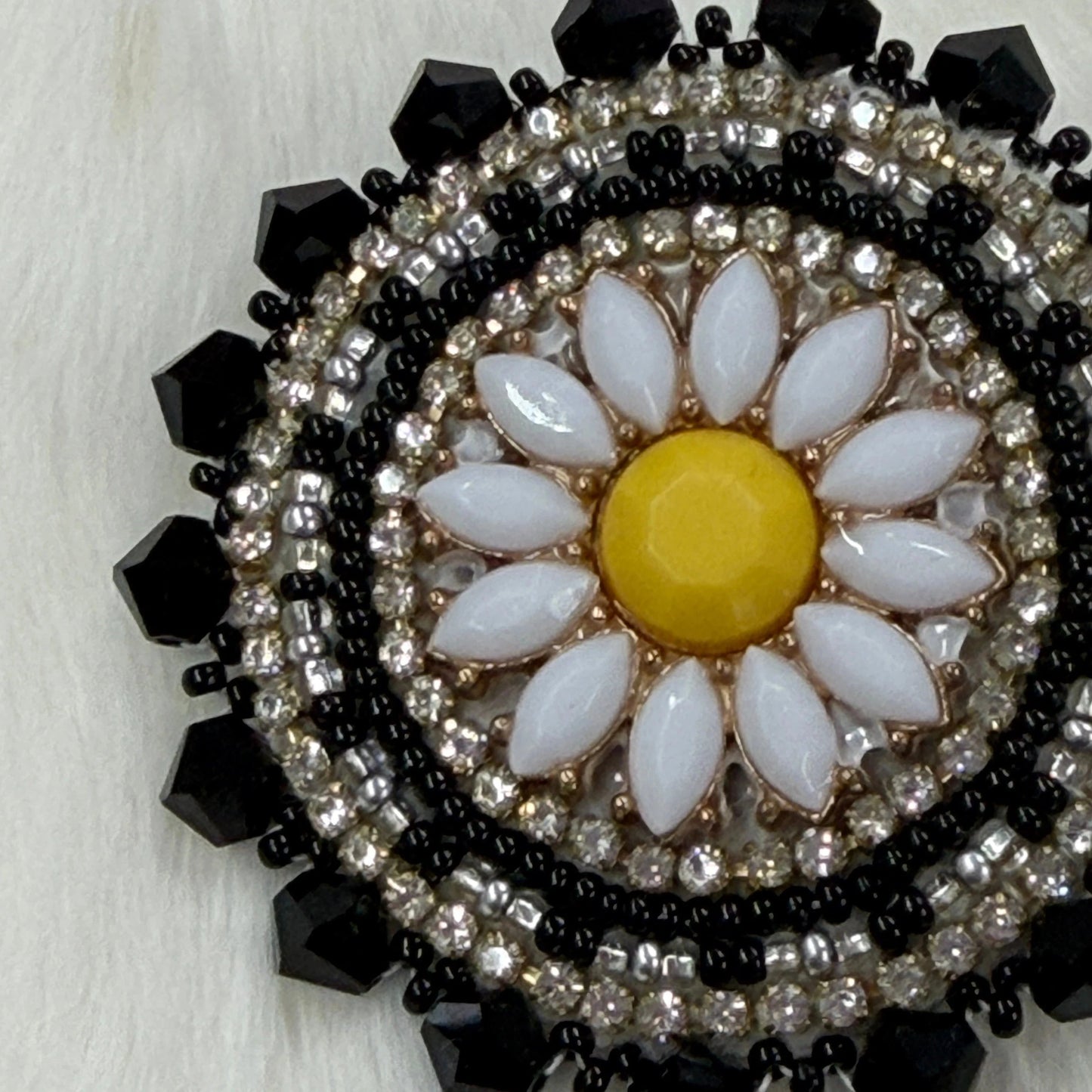Decorative brooch with floral design and black and silver beading on a light background