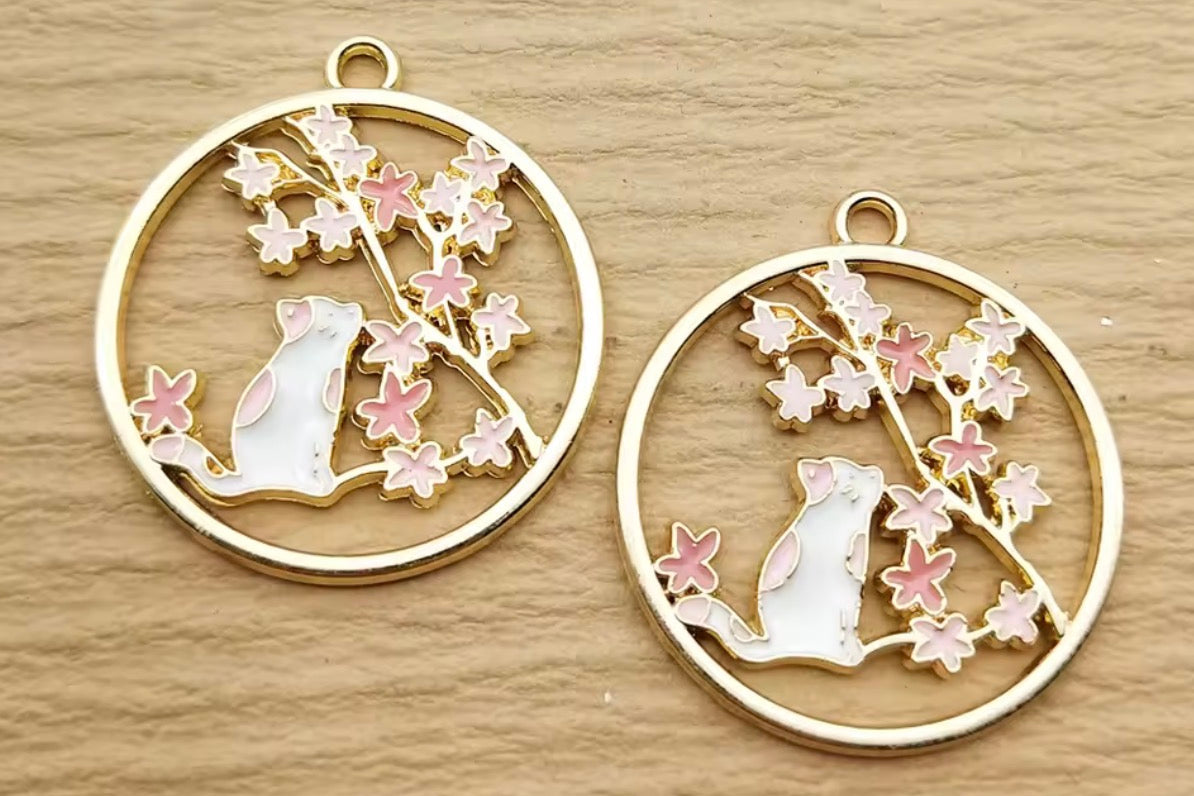 Two gold circular pendants with cat and flower designs on a wooden surface