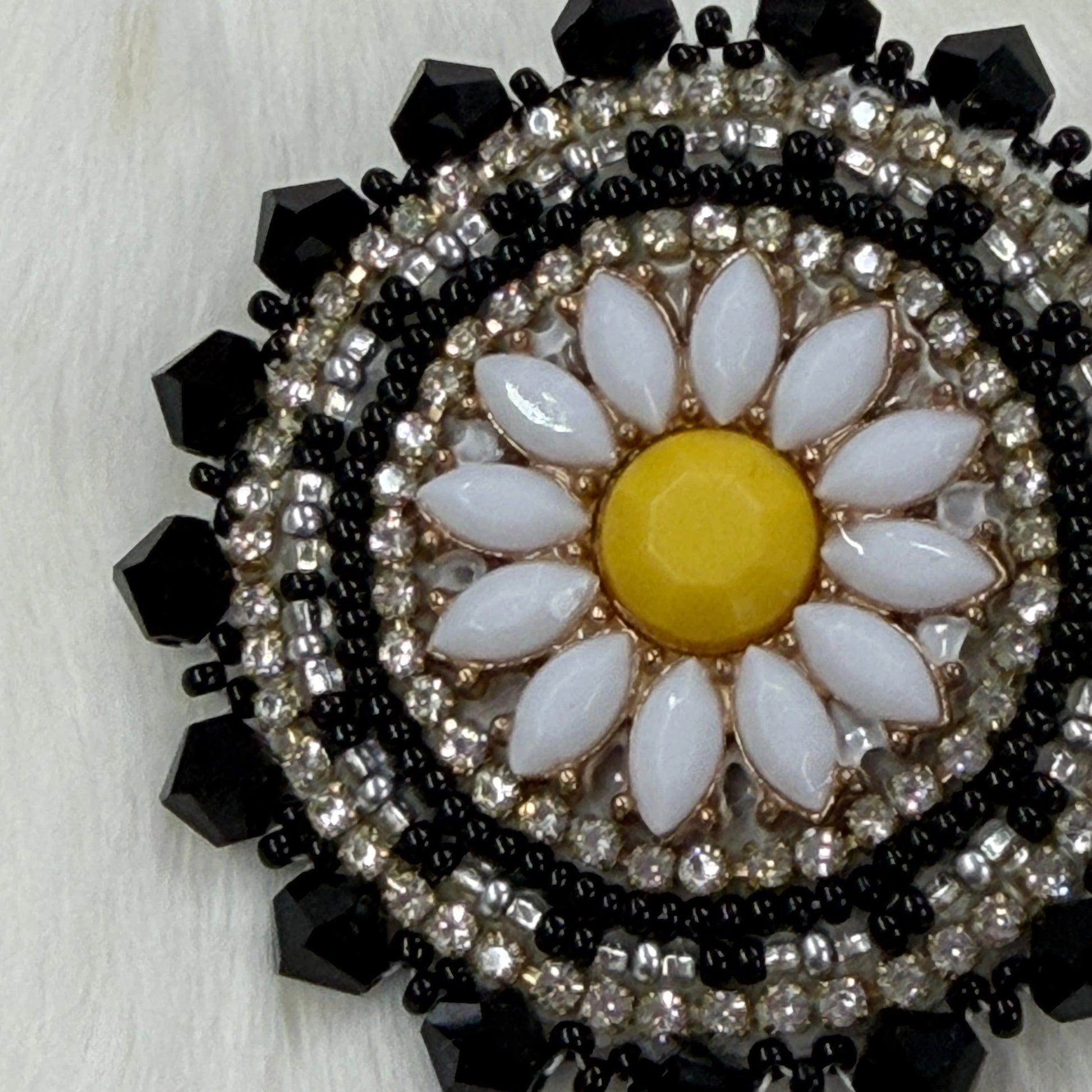 Decorative brooch with floral design and black and silver beading on a light background