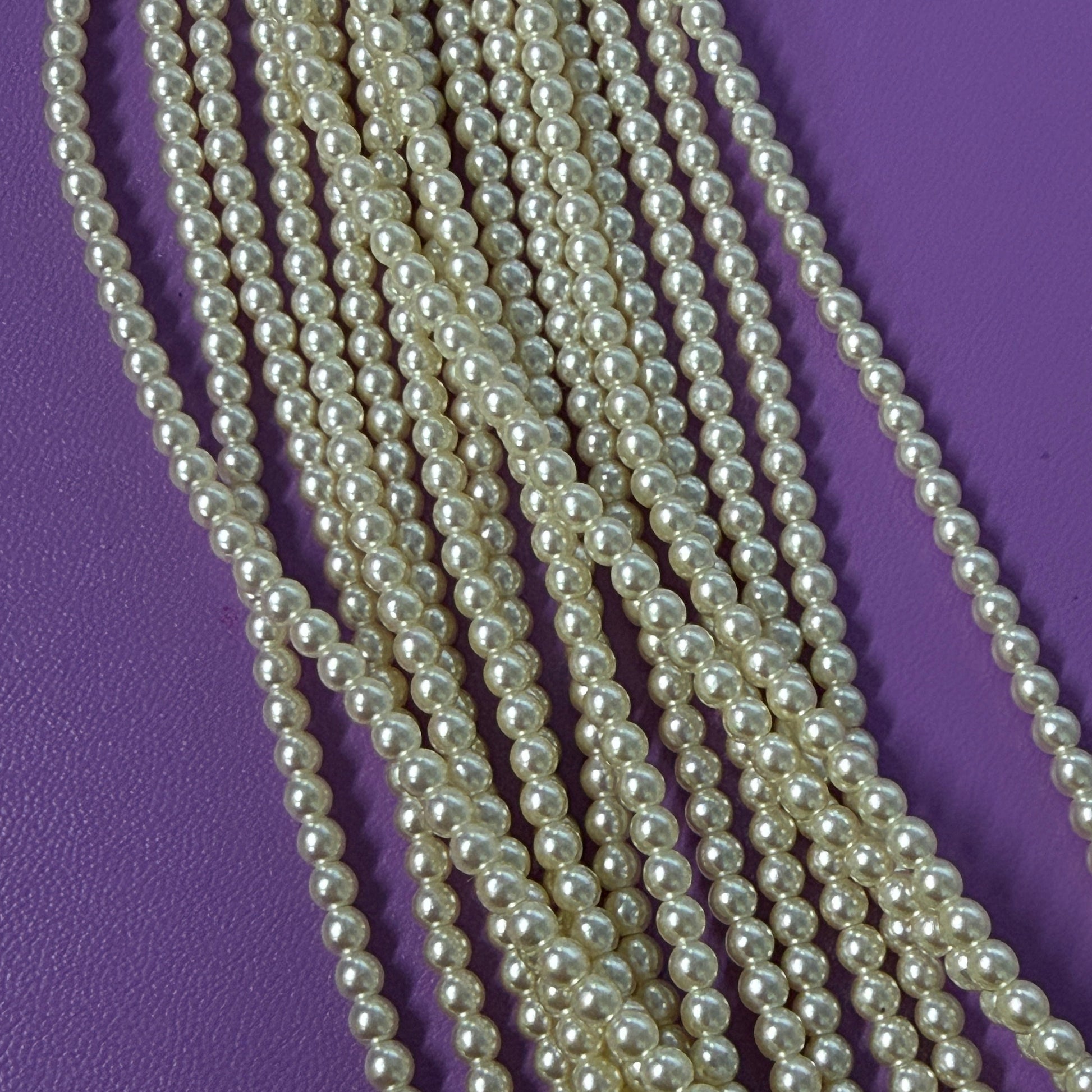 Multiple strands of pearl beads on a purple background
