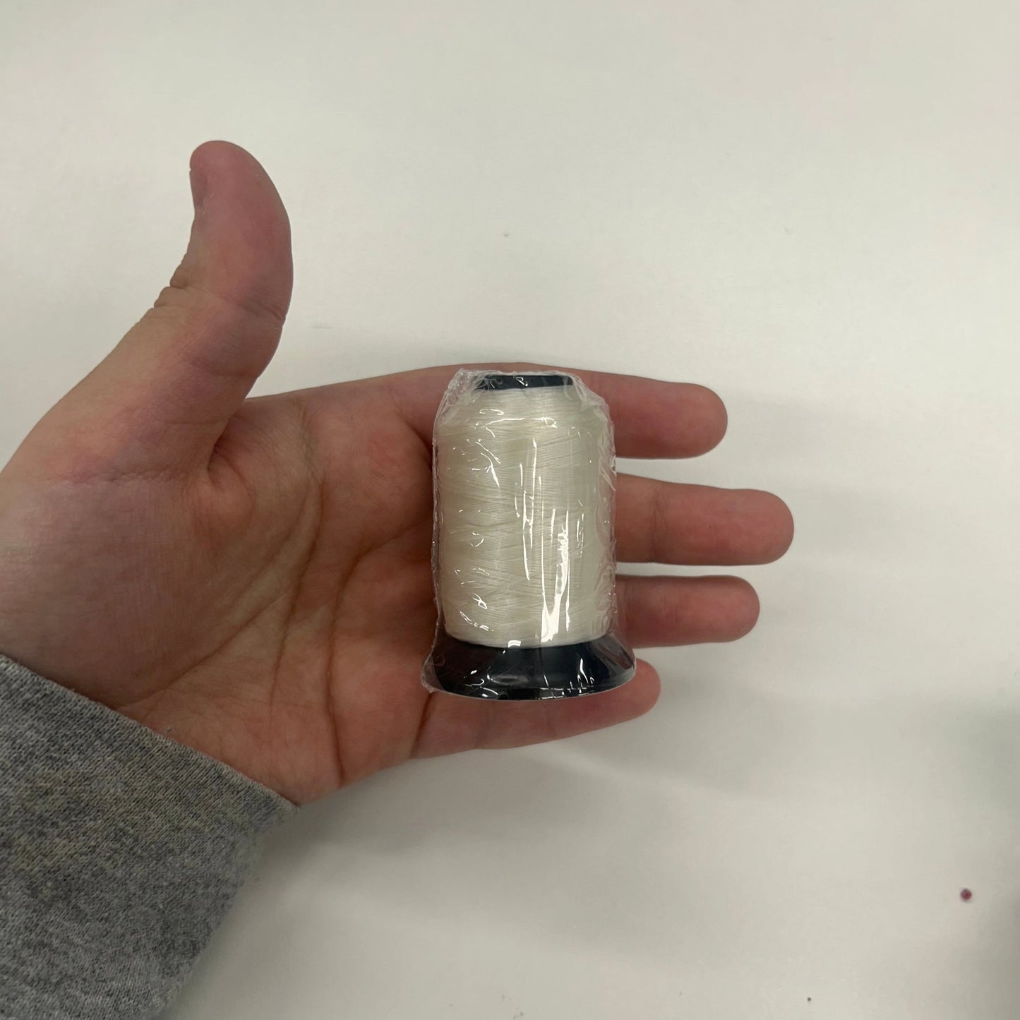 Hand holding a spool of thread against a white background