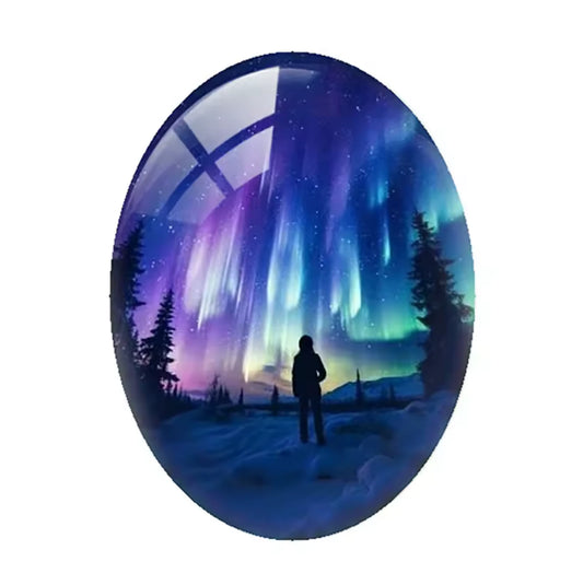 A glossy oval gemstone or cabochon featuring a printed design of a silhouetted figure standing in a snowy landscape under a vibrant purple and blue aurora borealis sky, shown on a white screen with a sidebar of thumbnail images.